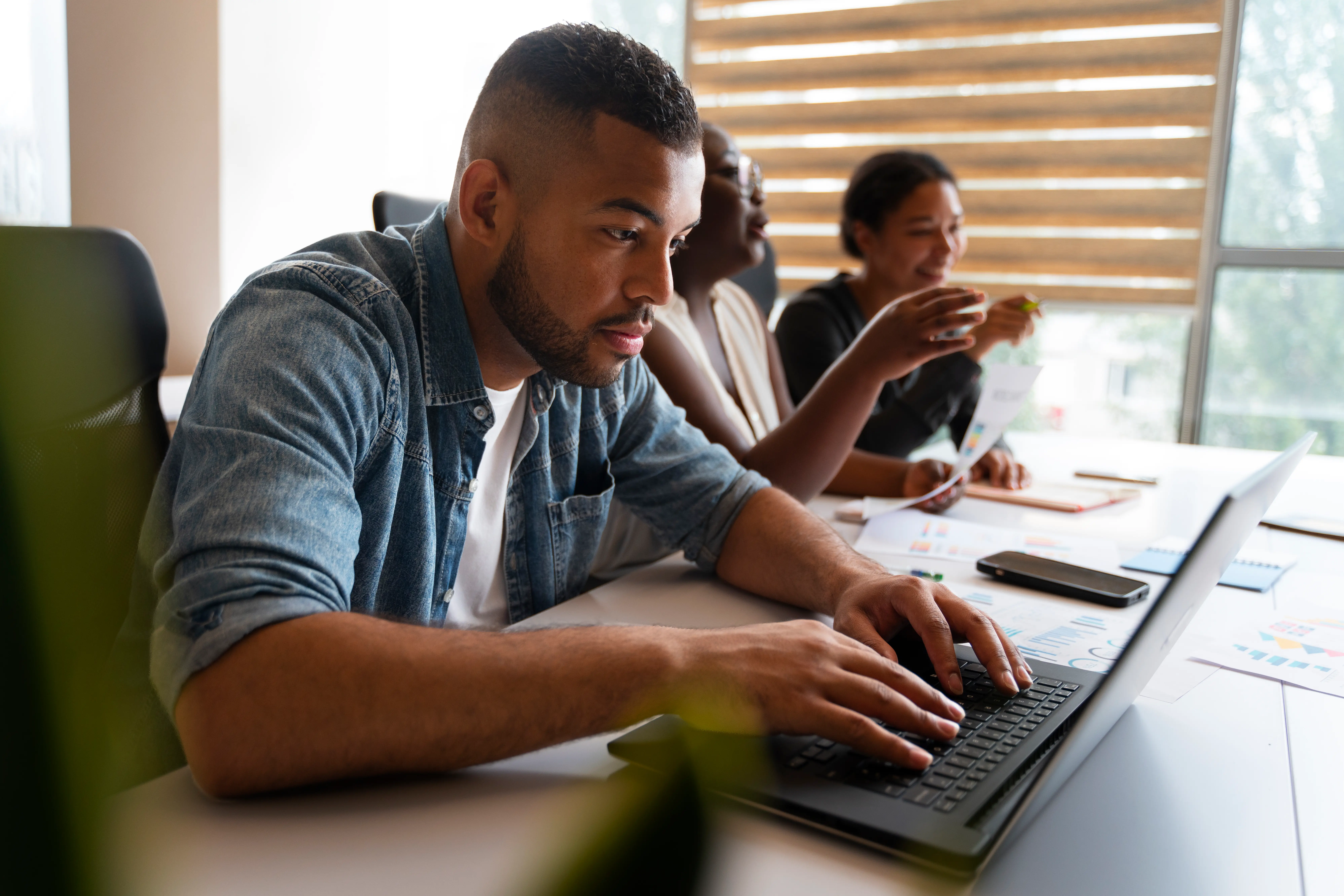 Professionnel concentré sur son ordinateur portable lors d'une formation SAP, accompagné de collègues échangeant sur des documents et graphiques d'analyse.