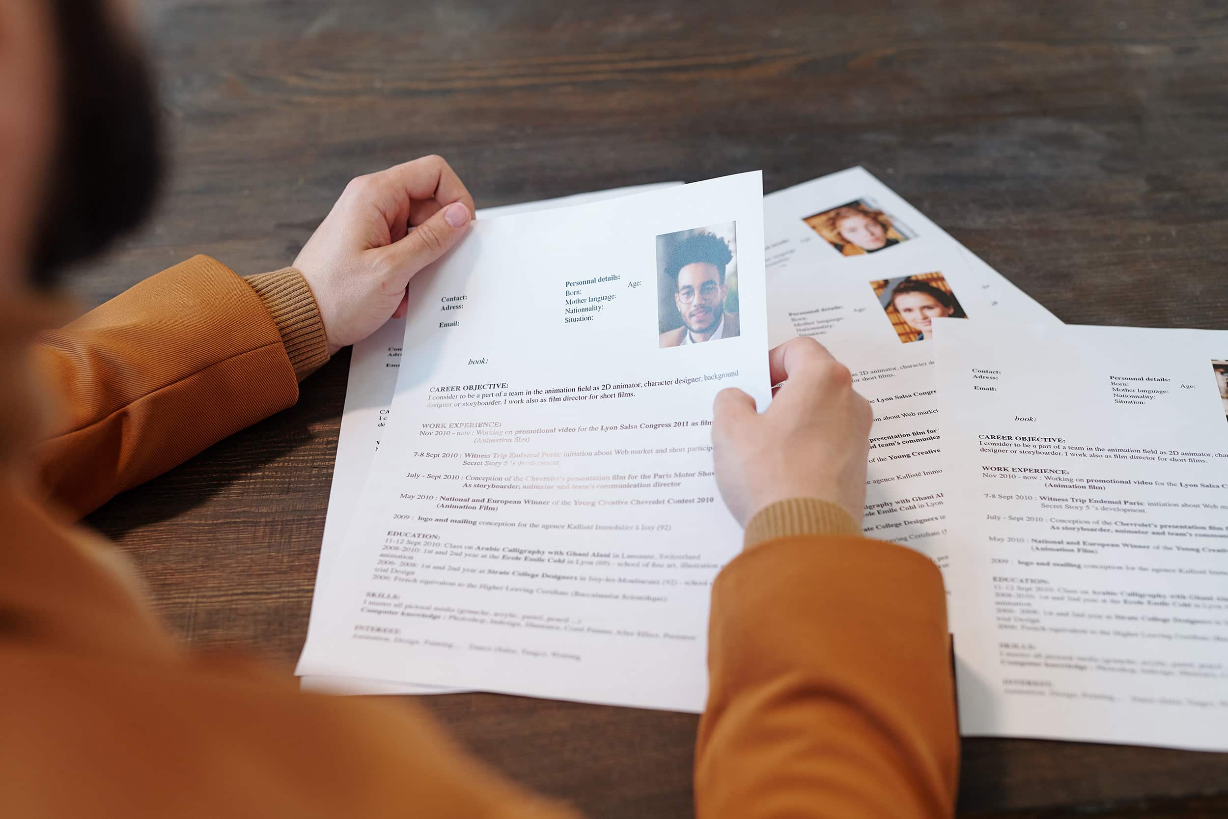 Une personne consulte plusieurs CV posés sur une table, illustrant le travail minutieux d’un cabinet de recrutement data dans la sélection de profils qualifiés pour des postes en entreprise.